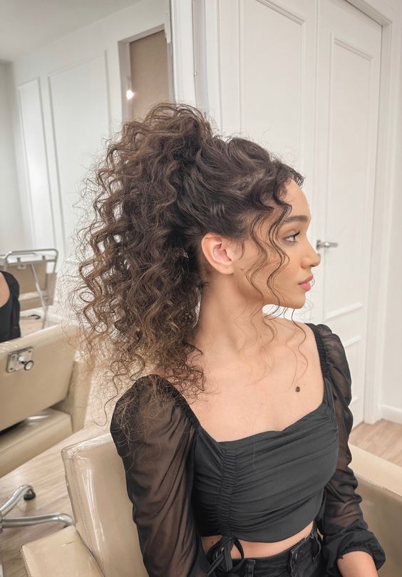 A woman with curly hair sitting in a chair, sporting a ponytail hairstyle