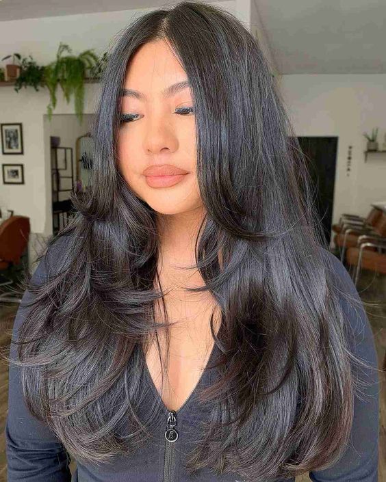 A woman with layered hair, wearing a blue top, and with long black hair framing her face.