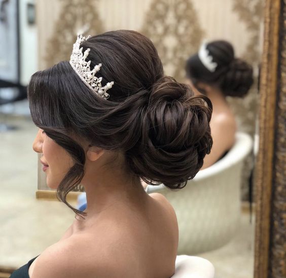 A woman wearing a quinceanera headpiece bun, getting her hair done in a salon